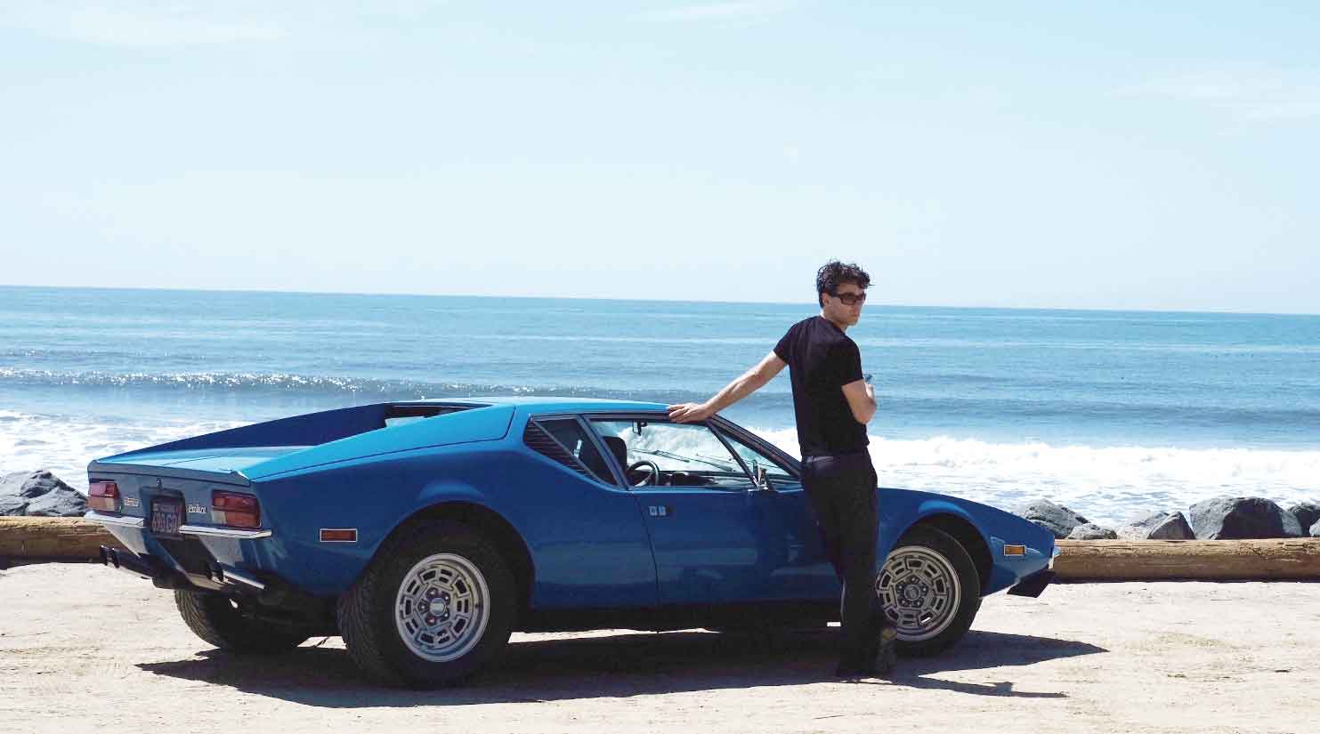 A man leaning on a blue Pantera beside the sea